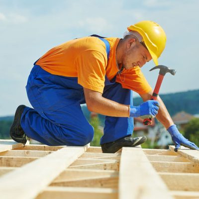 construction roofer carpenter worker nailing wood board with hammer on roof installation work
